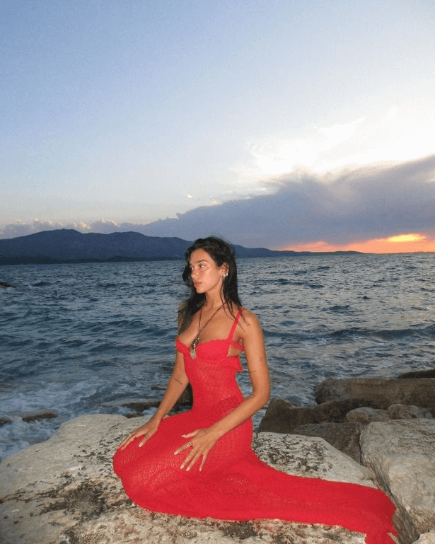 Taking to the beach in a sheer dress, Dua Lipa posed with her signature pout on a rock against the lush landscape in a series of seaside snaps.