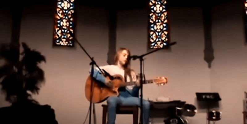 A different video shows Billie playing an acoustic guitar at her church, singing into a microphone with her hair in a darker shade of mouse brown.