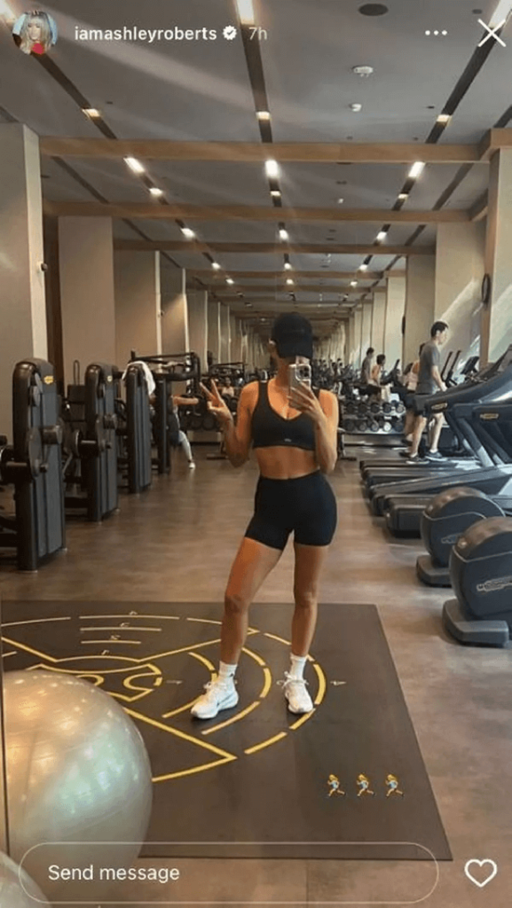 In the luxurious gym, Ashley wore a black sports bra and black cycling shorts that cinched her waist, paired with white tube socks and white sneakers as she threw up a peace sign.