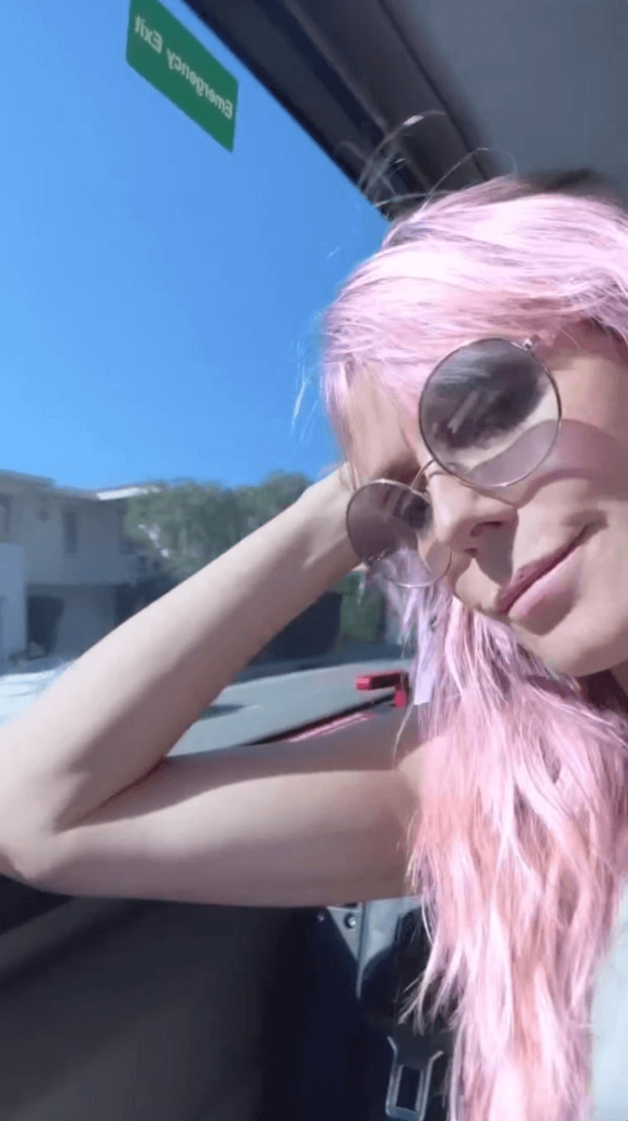 She turned and smiled at the camera, her eyes covered with her new pink hair, as she gazed out the window of a moving car, the Californian landscape visible outside.