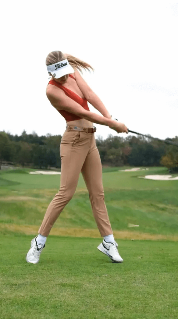Charis wears a red mid-drift, tan pants, and a white Titleist hat in the video. She captioned the post: "Fairway finder."