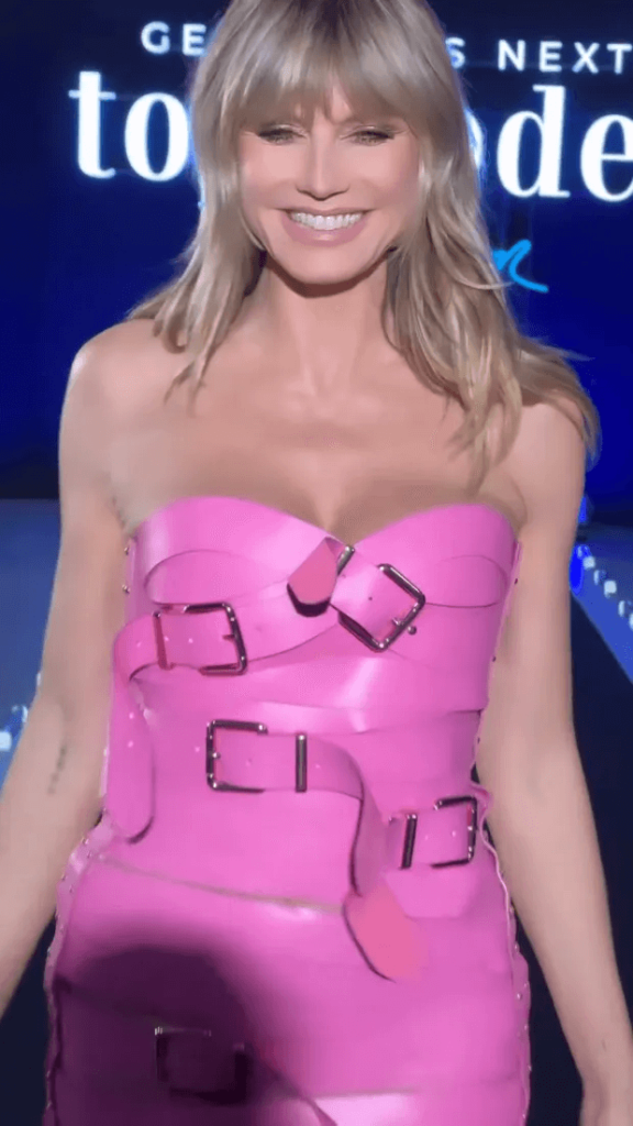 Her strapless dress surrounded by pink belts nearly blew out as she flaunted cleavage and strutted down the runway.