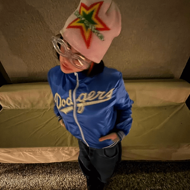 In a blue Dodgers jacket and baggy dark jeans, Billie pulled on a pastel pink woollen hat emblazoned with a star to cover her dark hair, and she added a pair of retro plastic glasses.
