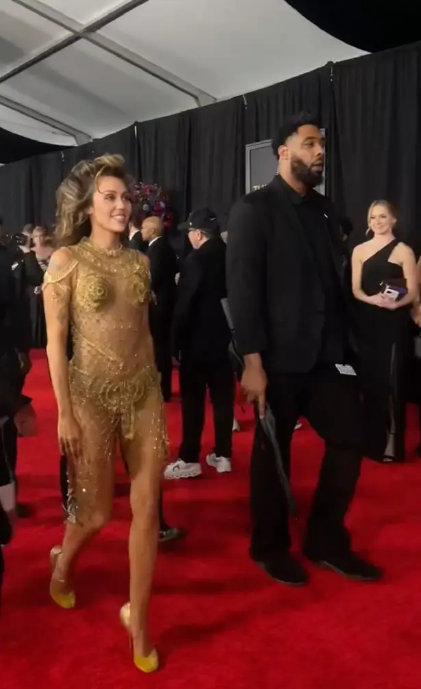 On the Grammys red carpet, Miley Cyrus wore a see-through gold gown, which distracted viewers after a woman walked alongside her covering her bum.