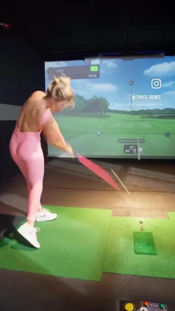 During the video, she is seen swinging her club at a ball, which then hits a screen with a virtual golf course projected onto it and lands.