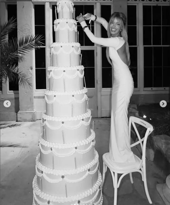 As the night progresses, Maura Higgins is seen playfully cutting a massive cake, a gesture that adds to the celebratory atmosphere. Guests eagerly await their turn to indulge in the delectable treat.