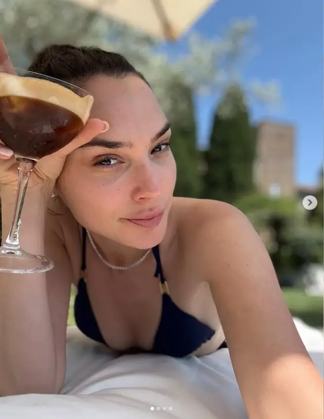 The image that garnered the most attention, though, was one where Gadot posed on her stomach. She donned a brown bikini top and grasped a glass of alcohol, her smile radiating a sense of contentment as she gazed up at the camera.
